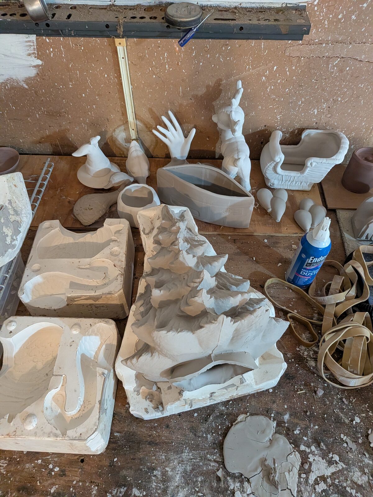 Alesha's workbench covered in plaster moulds, cast ceramic geese and pigs, unfired sprues and clay scraps, with a spirit level resting across the back.
