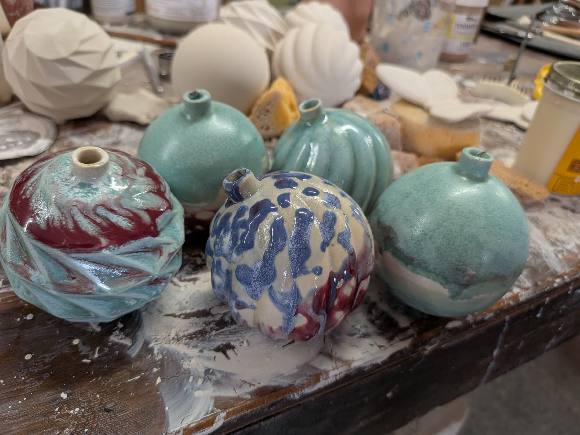 Round ceramic ornaments in muted teal and cream, marbled and striped with red and blue, standing on a splattered board.